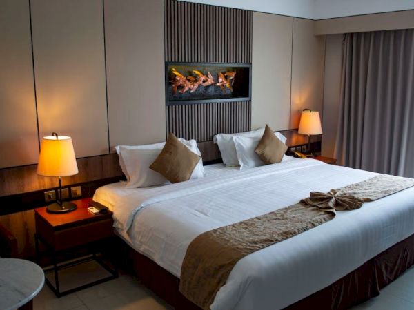 This image shows a neatly made hotel room bed with two side tables, lit lamps, and a modern wall design featuring a small in-wall fireplace.