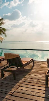 A serene view of a tropical poolside with lounge chairs, umbrellas, and palm trees overlooking a calm, sunlit ocean.