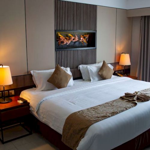 A neatly arranged hotel room with a large bed, two bedside tables with lamps, and a decorative wall panel behind the bed.