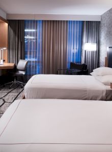A modern hotel room with two beds, a desk and chair, a wall-mounted TV, and stylish decor.