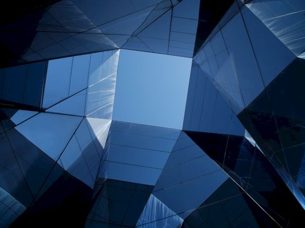 The image shows a geometric arrangement of reflective glass panels forming a symmetrical pattern with a view of the sky through the center.