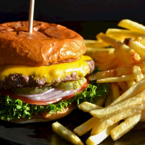 A cheeseburger with lettuce, tomato, and onion, paired with a side of crispy fries, served on a plate.
