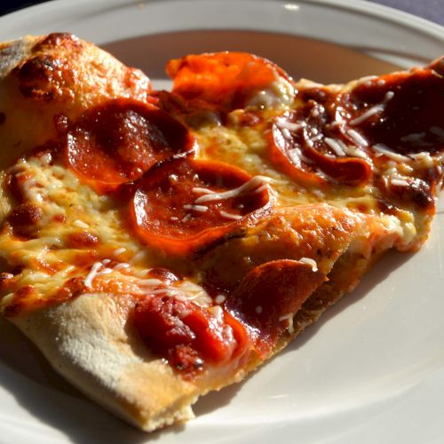 A slice of pepperoni pizza on a white plate, featuring melted cheese and crispy pepperoni slices.