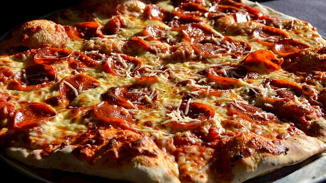 A large pepperoni and sausage pizza with melted cheese on a dark surface, sliced and ready to serve.