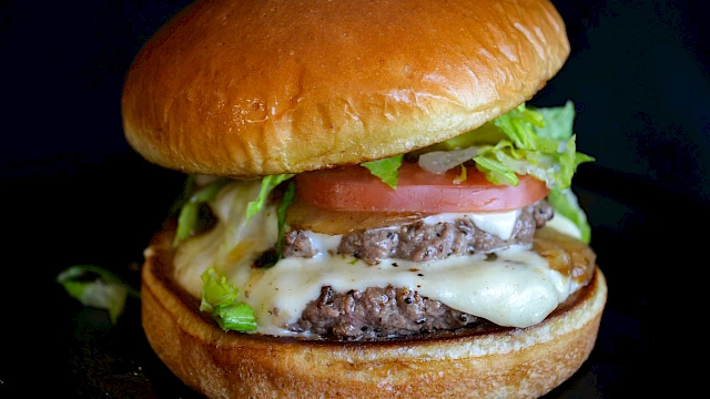 A juicy cheeseburger with a toasted bun, beef patty, melted cheese, lettuce, tomato, and pickles, all stacked high on a bun.