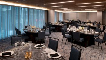 A spacious banquet hall with several round tables set for a formal event, decorated with neutral tones, centerpieces, and neatly folded napkins.