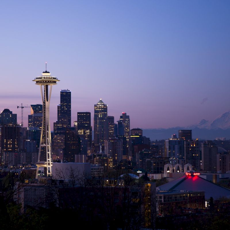 This image shows the Seattle skyline at dusk, with the Space Needle prominently visible and Mt. Rainier in the background, bathed in twilight hues.