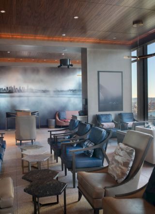 A modern lounge area with comfortable seating, large windows offering a scenic view of a waterfront and ferris wheel, and a mural of a city skyline.