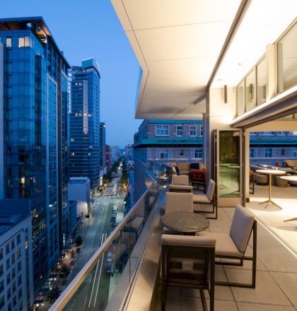 A modern balcony view of a cityscape at dusk, showing high-rise buildings and an elegantly furnished outdoor seating area.