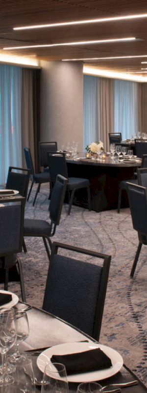 A banquet hall set up with round tables, elegant place settings, floral centerpieces, and modern lighting, ready for an event or gathering.