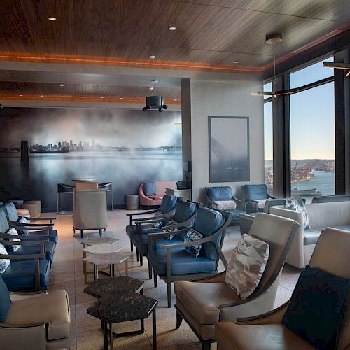 A modern lounge area features comfortable seating with views of a scenic waterfront and a Ferris wheel in the background through large windows.