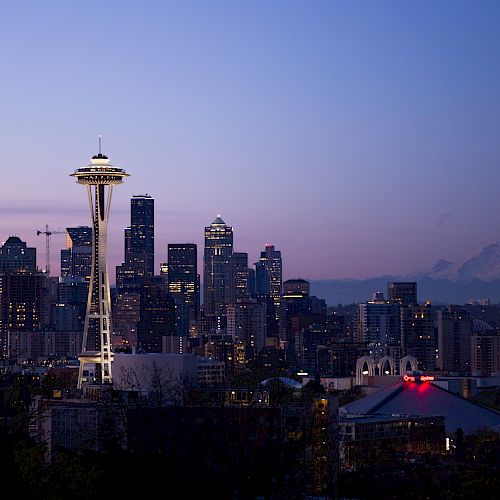 The image shows the Seattle skyline at dusk, featuring the Space Needle prominently and Mount Rainier in the background.