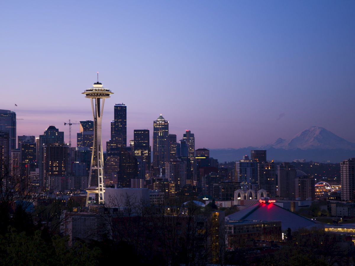 This image shows the Seattle skyline at dusk, including the Space Needle and Mount Rainier in the background, under a clear sky.