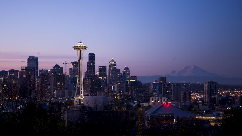 This image shows the Seattle skyline at dusk, including the Space Needle and Mount Rainier in the background, under a clear sky.