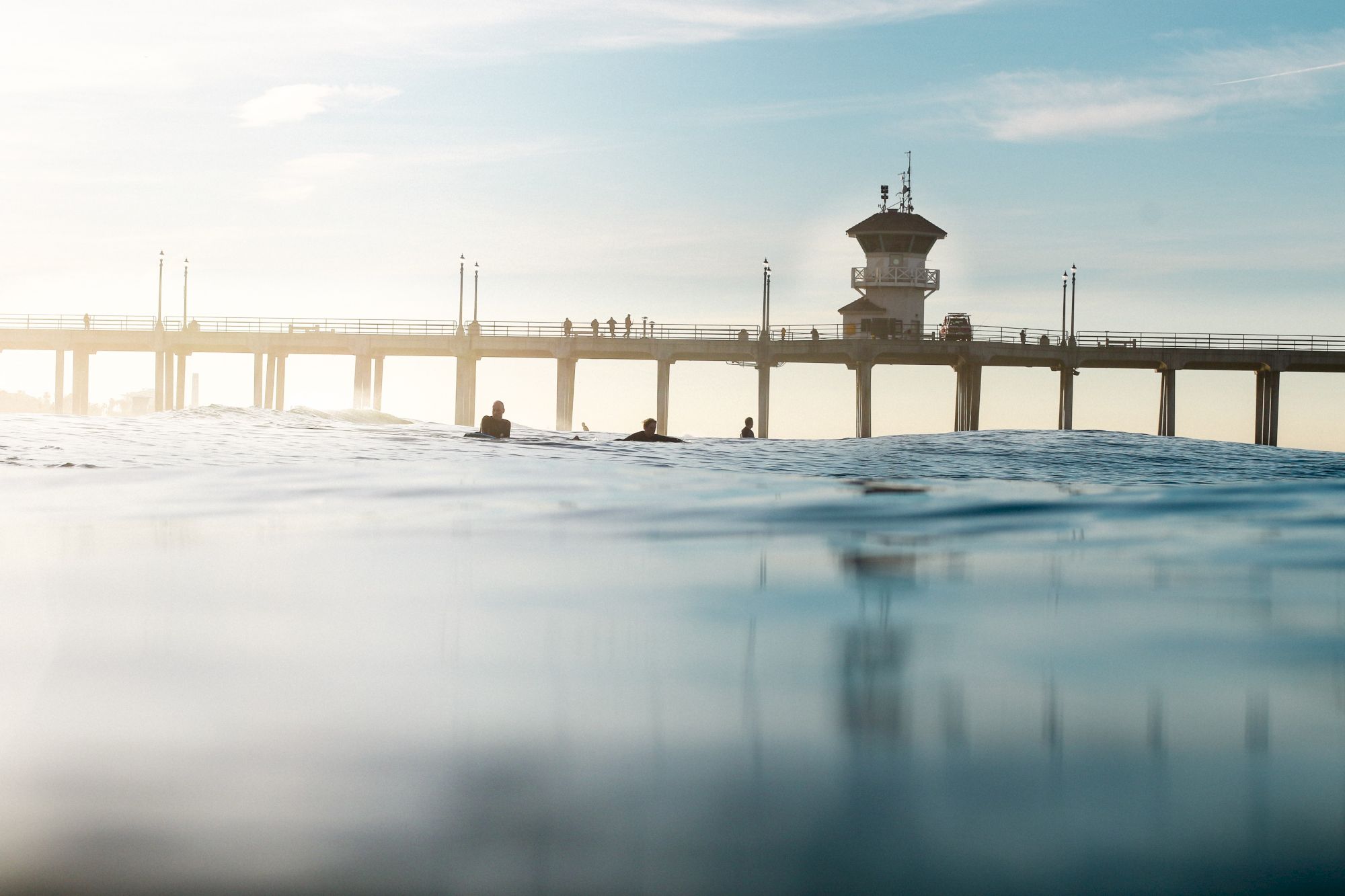 A serene image of people near a calm ocean, with a pier and a structure in the background stretching into the horizon ending the sentence.